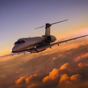 A luxury private jet overflying cloudy skies at sunset