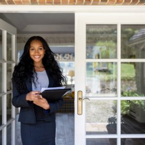 Portrait of an African American real estate agent at the door of a house for sale and looking at the camera smiling