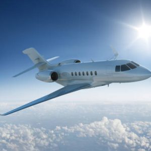 Private jet flies past sun - in blue sky above the clouds